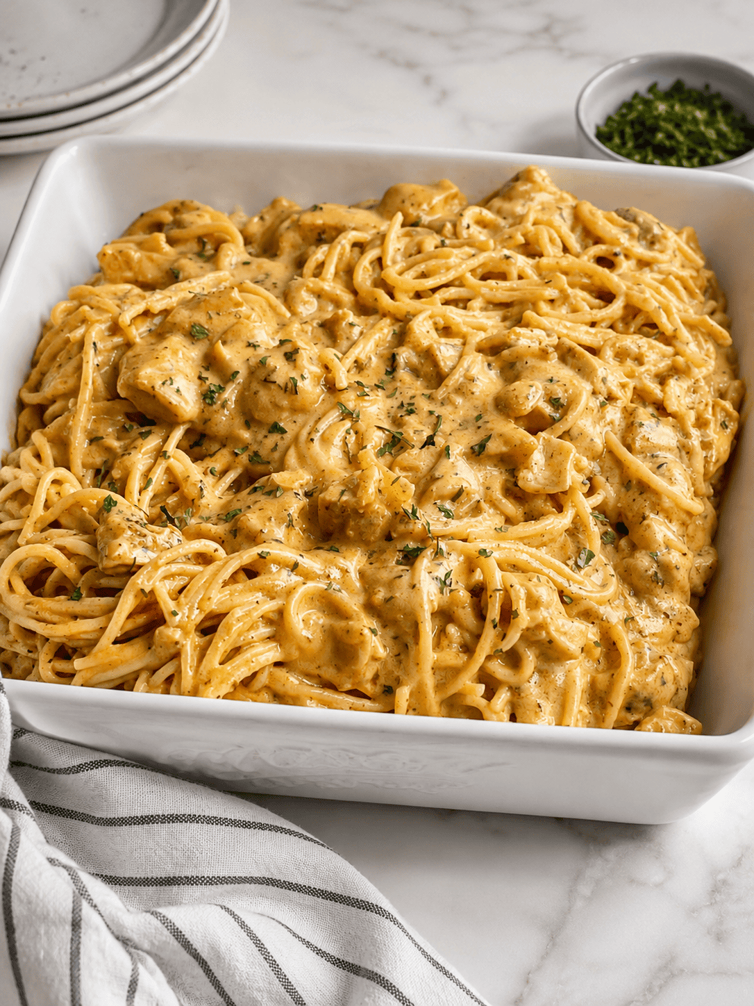 Creamy chicken spaghetti with tomato sauce and tender chicken pieces served in a white baking dish on a marble countertop.