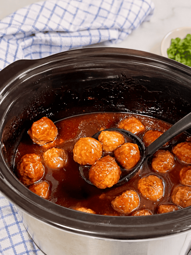 Close-up of juicy grape jelly meatballs coated in a glossy sweet BBQ sauce inside a slow cooker. These tangy grape jelly meatballs make the perfect easy appetizer or party snack.