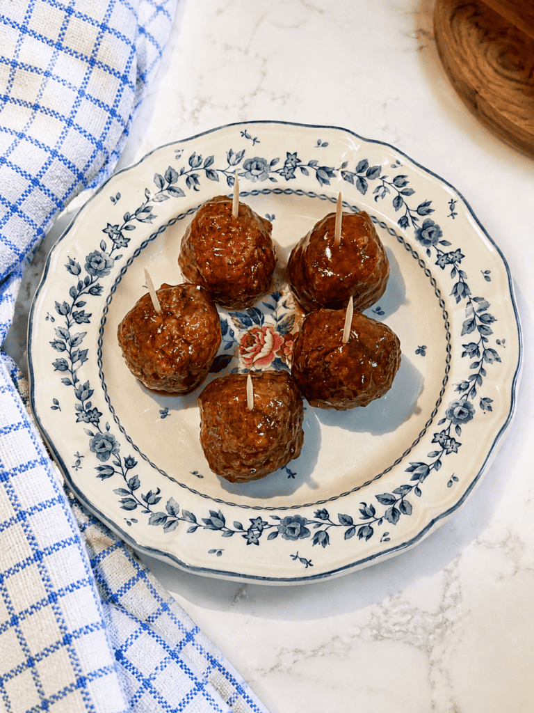Grape jelly meatballs served as bite-sized appetizers with toothpicks on a decorative plate. These crockpot BBQ grape jelly meatballs are a classic party appetizer for holidays and game day gatherings.