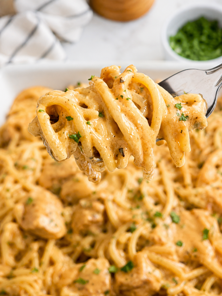 Forkful of creamy chicken spaghetti with tomato sauce, melted cheese, and tender chicken pieces lifted above the pasta dish.