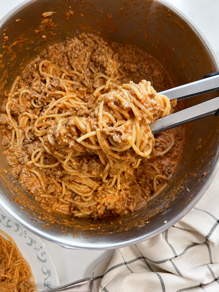 Creamy cheesy ground beef spaghetti being tossed in a large pot with rich tomato sauce, melted cream cheese, pepper jack cheese, and tender spaghetti noodles.