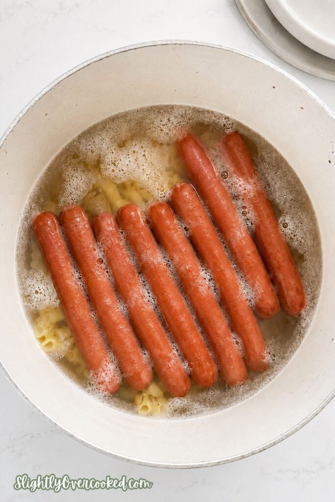 Hot dogs boiling with macaroni noodles in a pot while preparing an easy family dinner