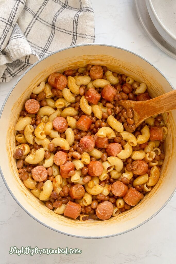 Creamy macaroni and cheese mixed with sliced hot dogs and country-style baked beans in a bowl