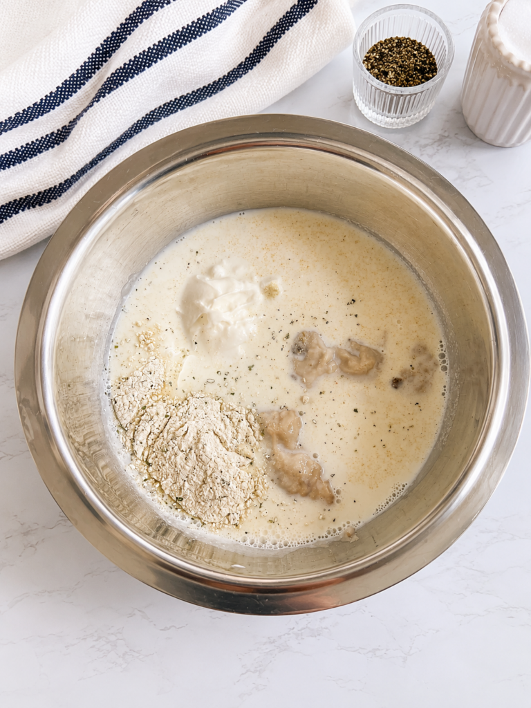 Cream of mushroom soup, milk, sour cream, ranch seasoning, onion powder, salt, and black pepper combined in a mixing bowl for creamy bacon ranch chicken.