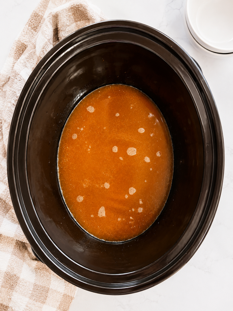 Sweet and savory baked bean sauce made with chicken broth, ketchup, brown sugar, molasses, Worcestershire sauce, and seasonings mixed in a slow cooker.