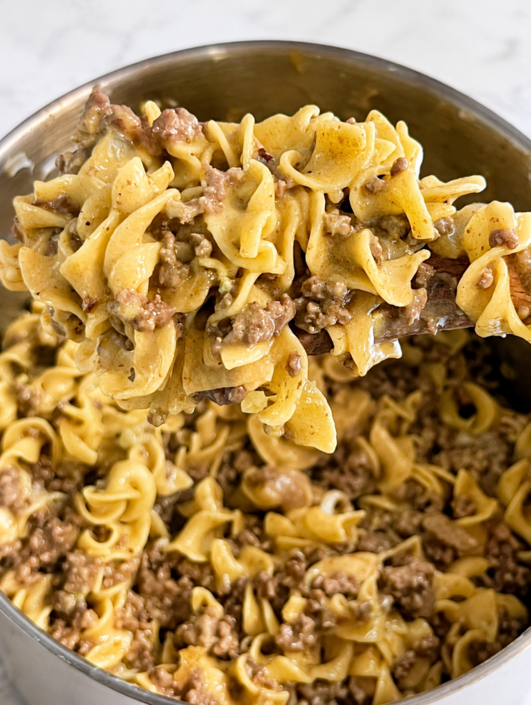 Close-up of creamy beef stroganoff with ground beef and tender egg noodles served from a skillet on a wooden spoon. This classic beef stroganoff recipe features a rich mushroom sauce made with beef broth, sour cream, Worcestershire sauce, and seasonings for an easy homemade comfort food dinner the whole family will love.