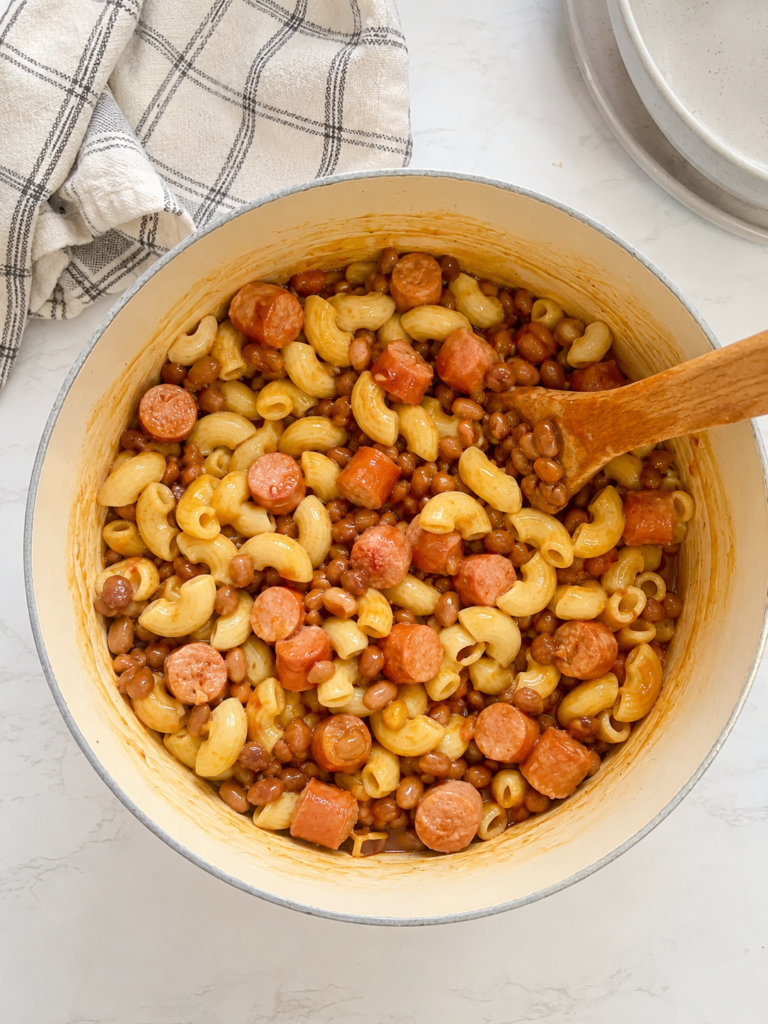 Creamy macaroni and cheese mixed with sliced hot dogs and country-style baked beans in a bowl