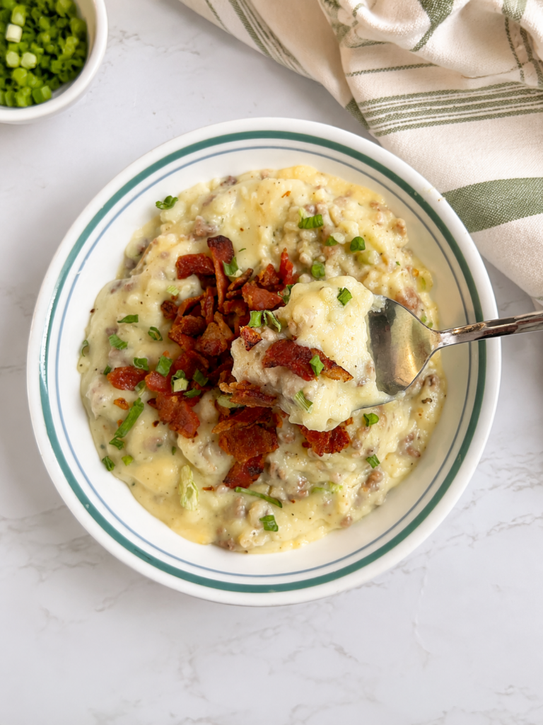 Creamy loaded baked potato casserole with ground beef, crispy bacon, cheese, and green onions, shown with a spoonful being served.