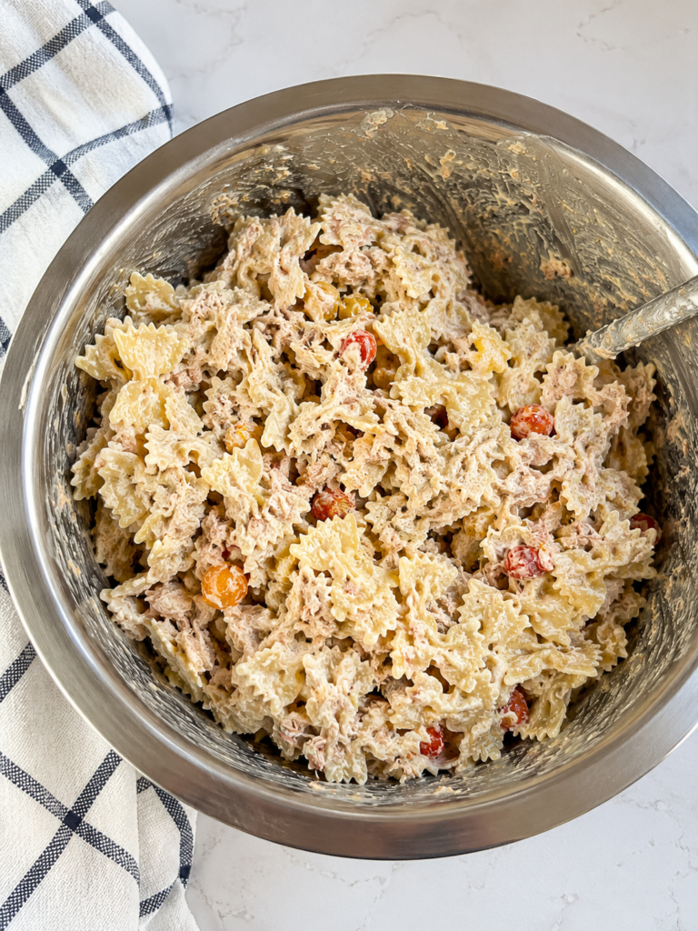 Classic tuna pasta salad featuring bowtie pasta, flaky tuna, creamy mayonnaise dressing, and juicy cherry tomatoes in a large mixing bowl, an easy make-ahead side dish for BBQs and potlucks.