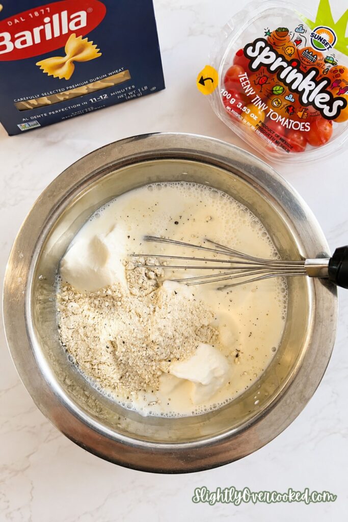 Creamy ranch dressing ingredients including milk, sour cream, and ranch seasoning whisked together for an easy pasta salad.