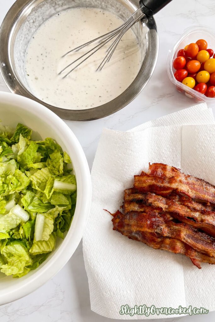 Creamy ranch dressing, crispy bacon, chopped romaine lettuce, and cherry tomatoes prepared for an easy bacon pasta salad recipe.