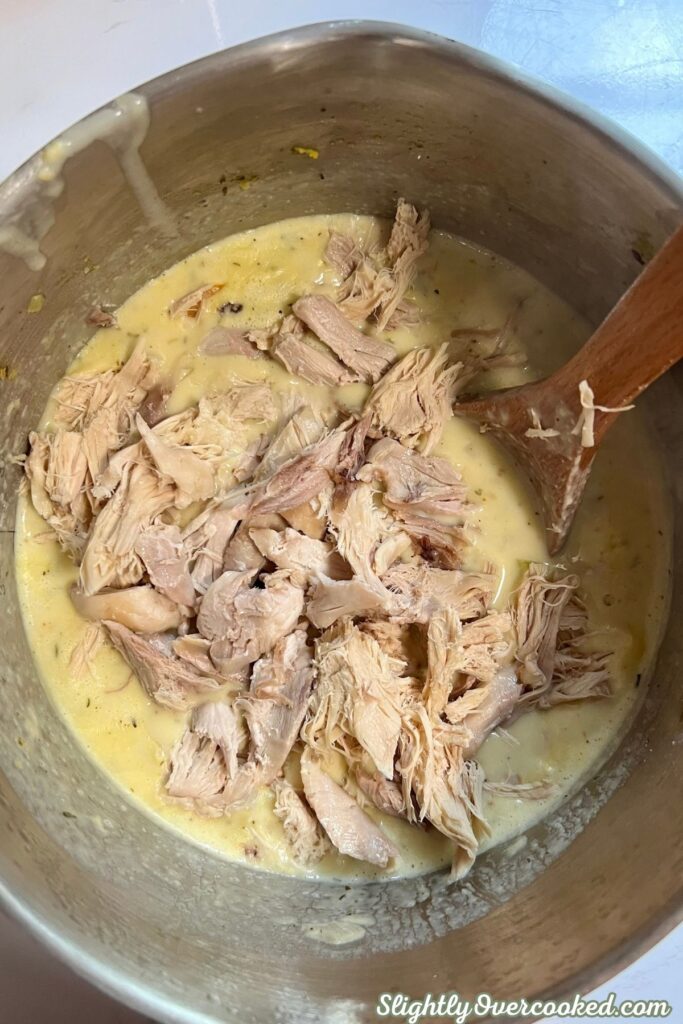 Shredded cooked chicken added to creamy broth for homemade chicken and dumplings