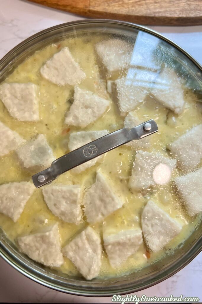 Biscuit dumplings covered with a glass baking lid over creamy chicken and vegetables