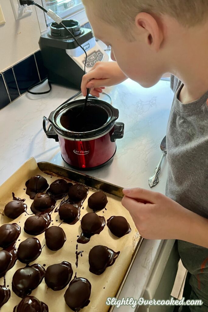 Homemade Oreo balls being coated in melted chocolate on a parchment-lined baking sheet