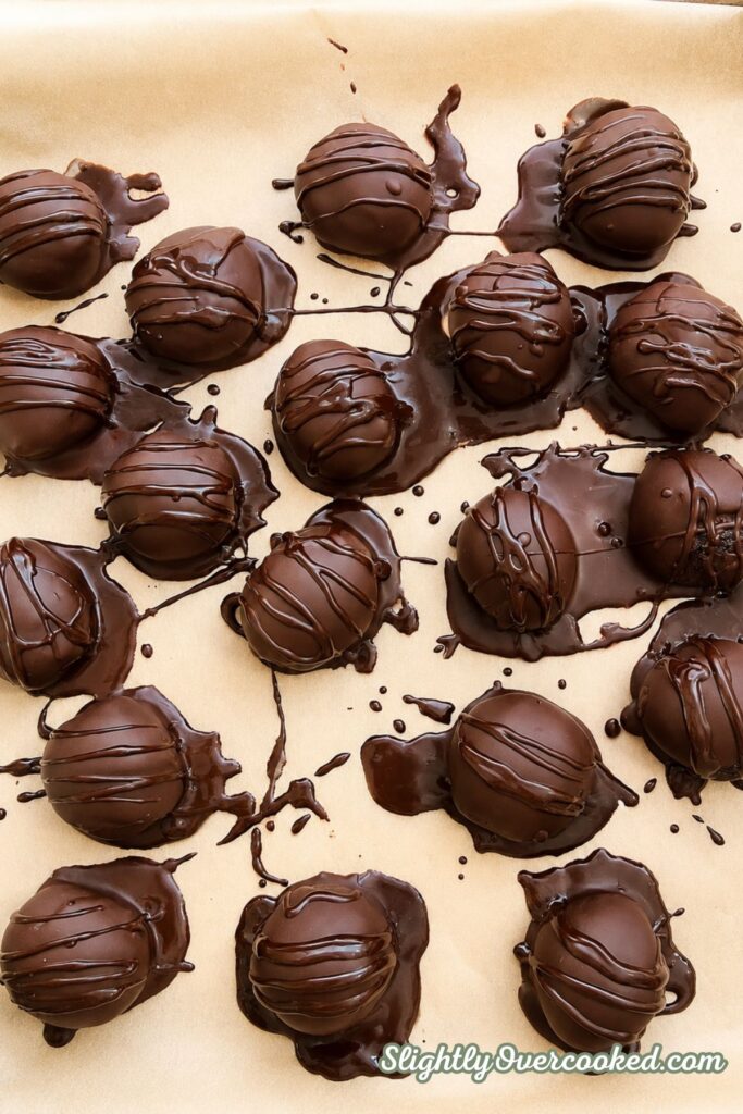 Homemade Oreo truffles coated in chocolate and drizzled with melted chocolate on a parchment-lined baking sheet