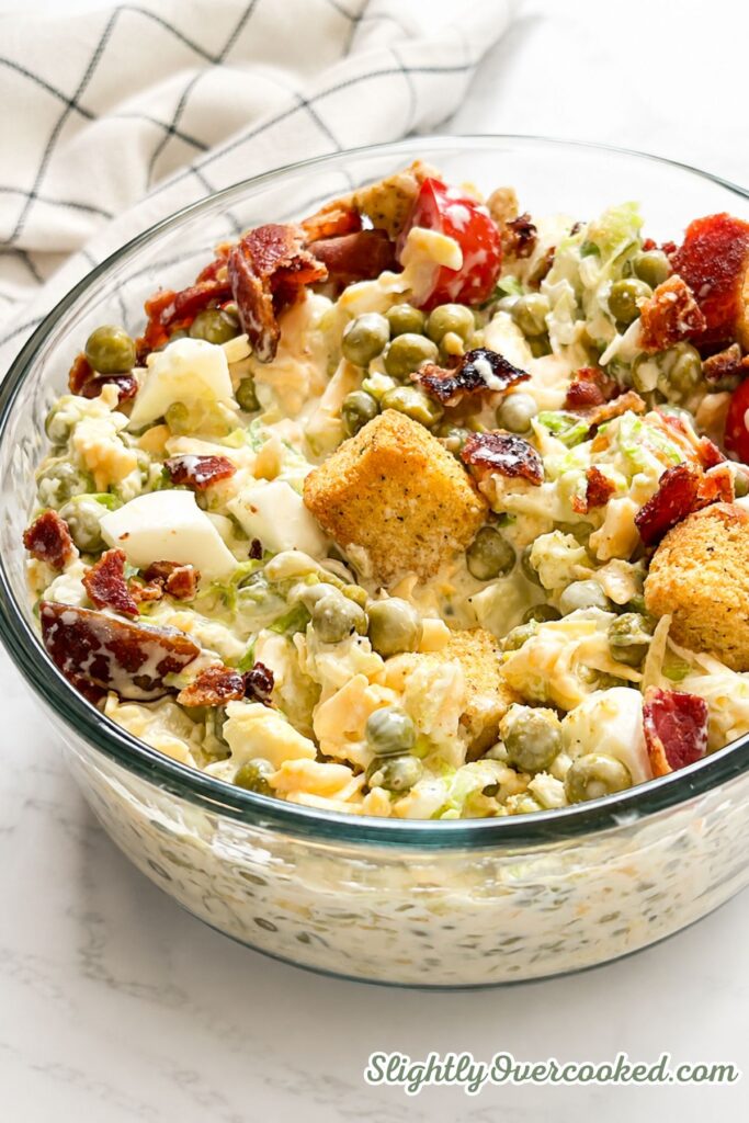Homemade pea salad tossed together in a large bowl with vegetables, cheese, eggs, and creamy dressing