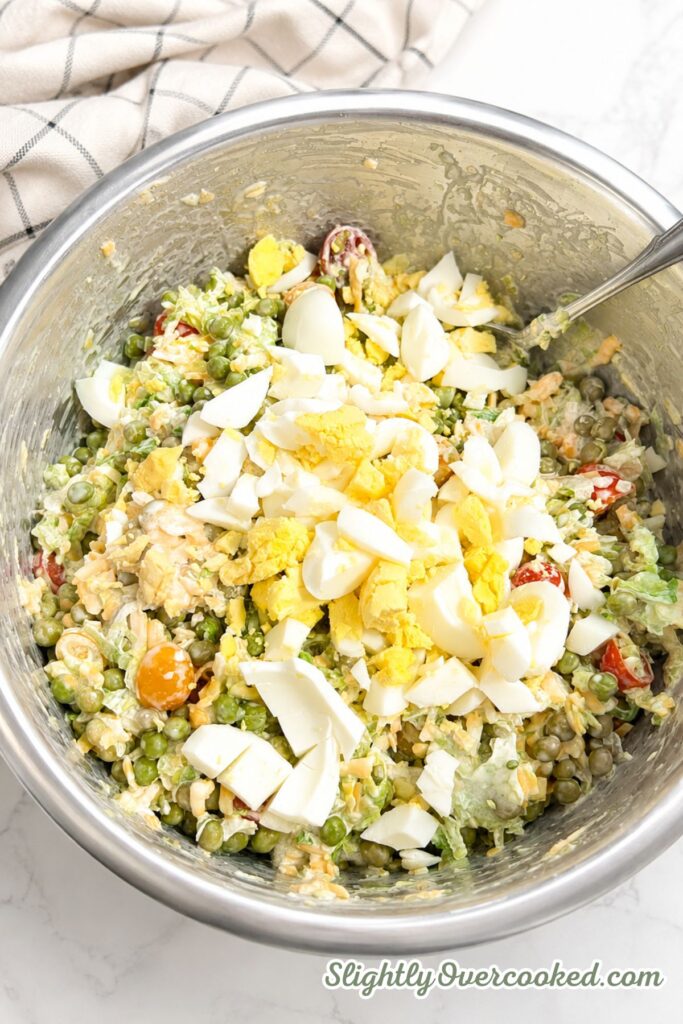 Chopped hard-boiled eggs added to a creamy mixture of peas, lettuce, cheddar cheese, bacon, and tomatoes
