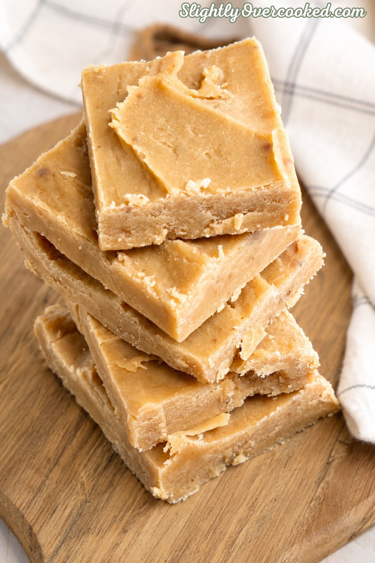 Stack of creamy homemade peanut butter candy squares on a wooden cutting board with a farmhouse kitchen towel