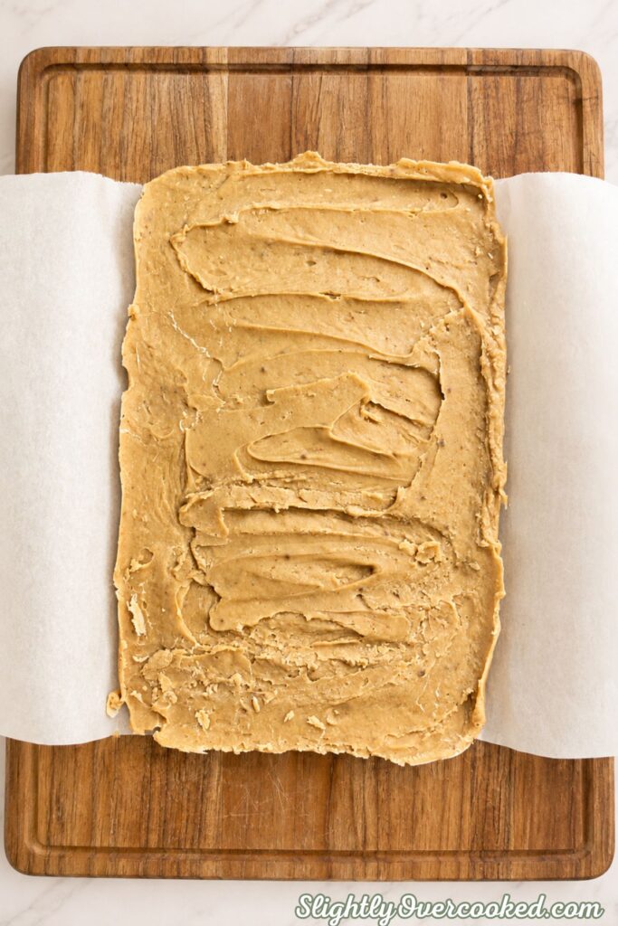 Peanut butter candy mixture spread evenly in a parchment-lined baking pan