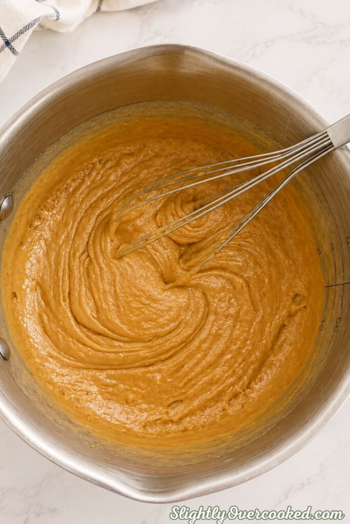 Thick peanut butter mixture being stirred in a saucepan until creamy