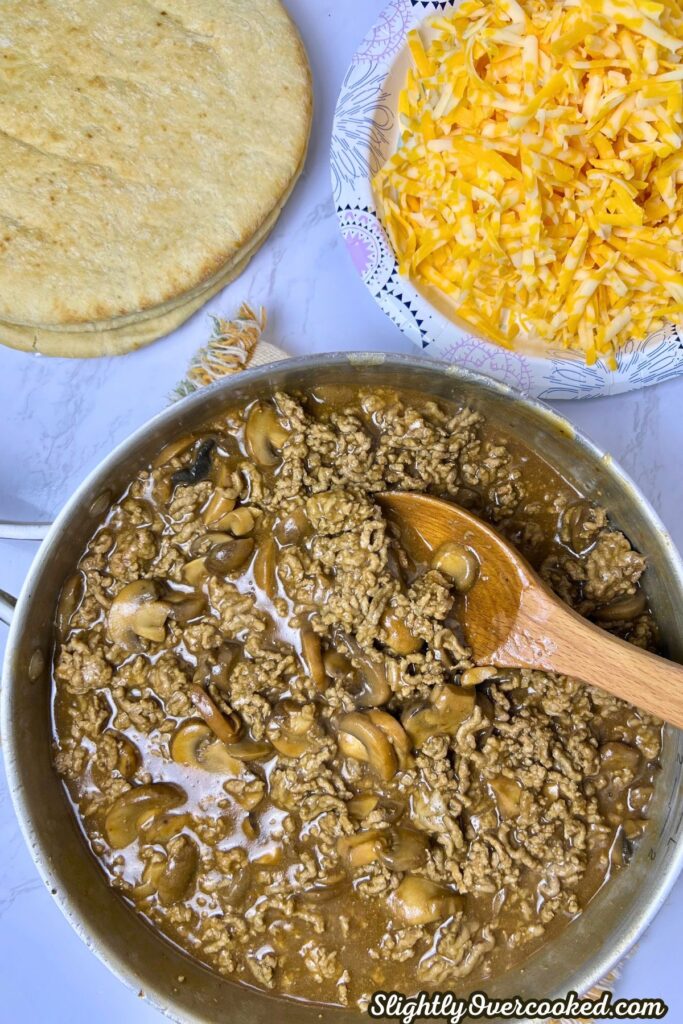 ground beef and gravy mixed together next to pita bread and cheese.