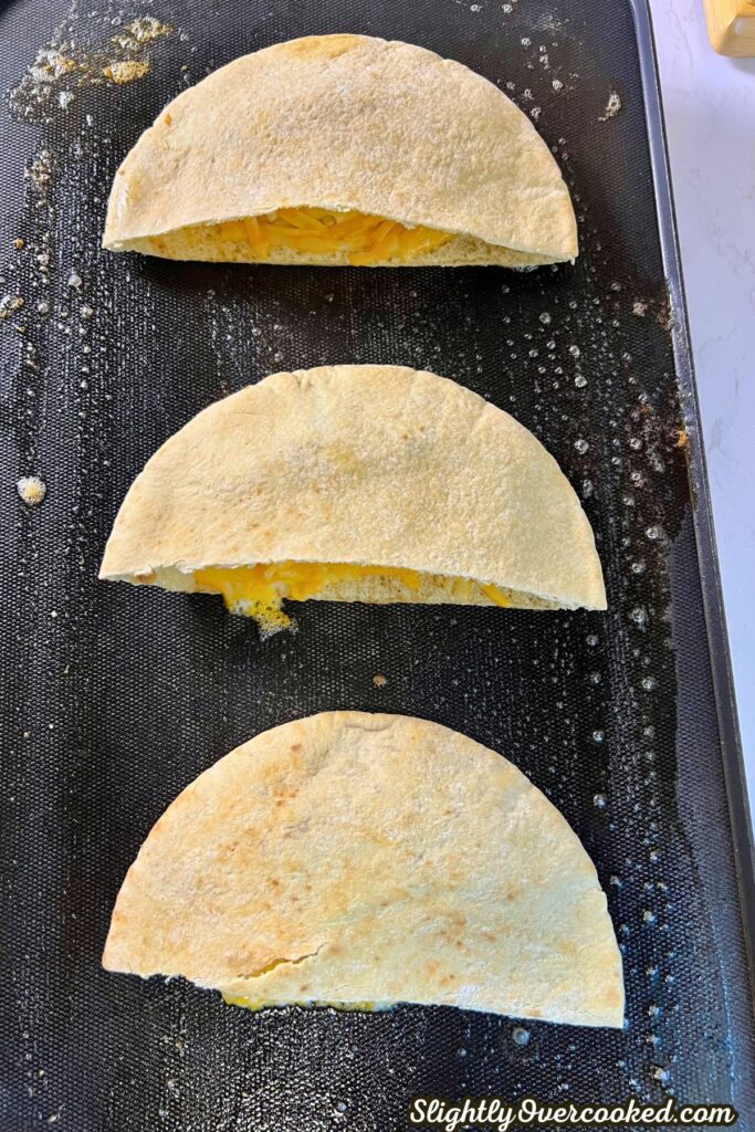 3 pita bread pockets cooking on a griddle.