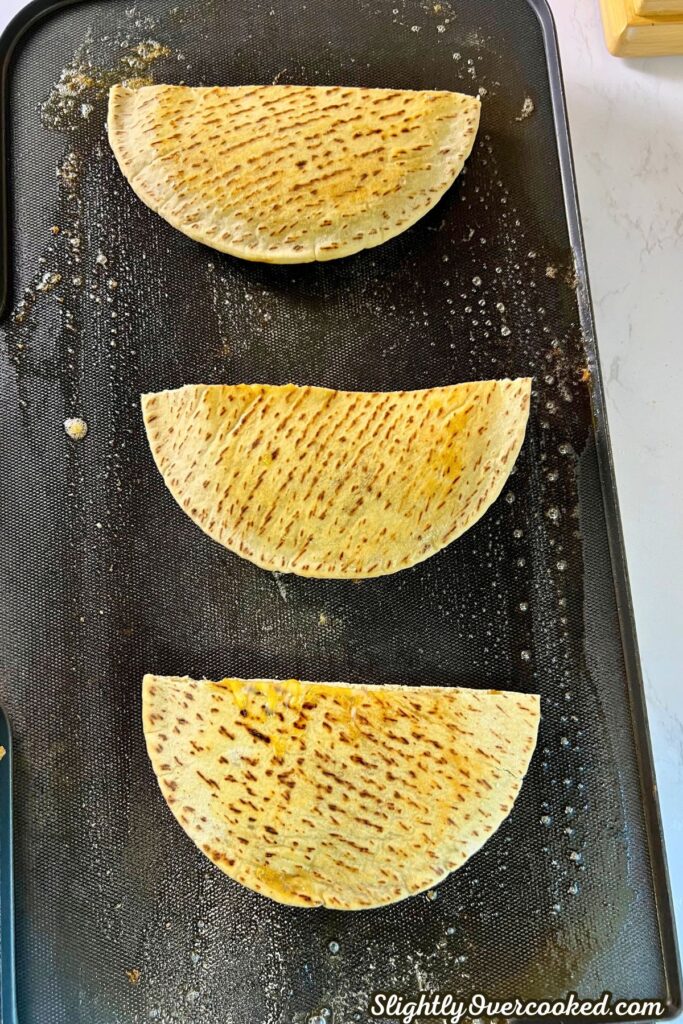 3 pita bread quesadillas cooking on griddle.